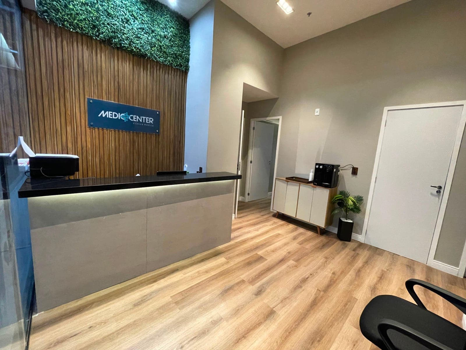 Balcão de recepção da Mediccenter, com painel ripado de madeira e o logo da clínica
